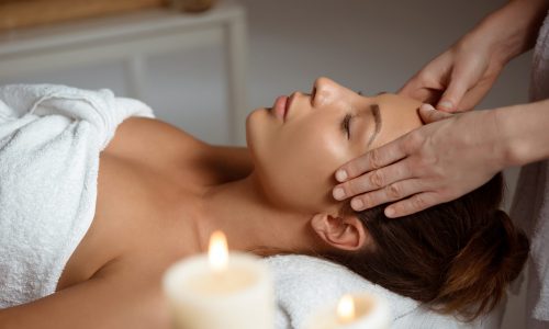 Young beautiful brunette girl having face massage relaxing in spa salon. Eyes closed. Copy space.